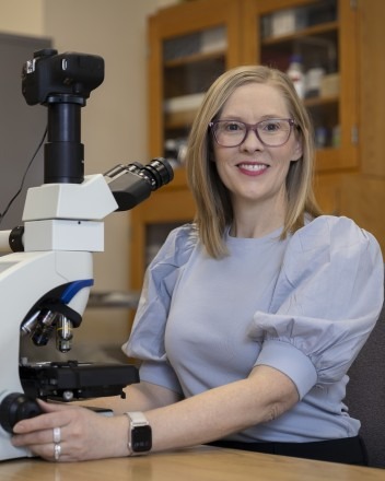 Faculty member smiling and sitting in front of a microscope